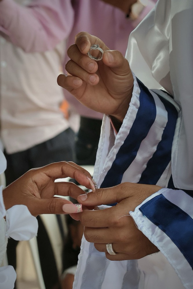 Two hands exchanging a ring beneath a tallit, a Jewish prayer shawl